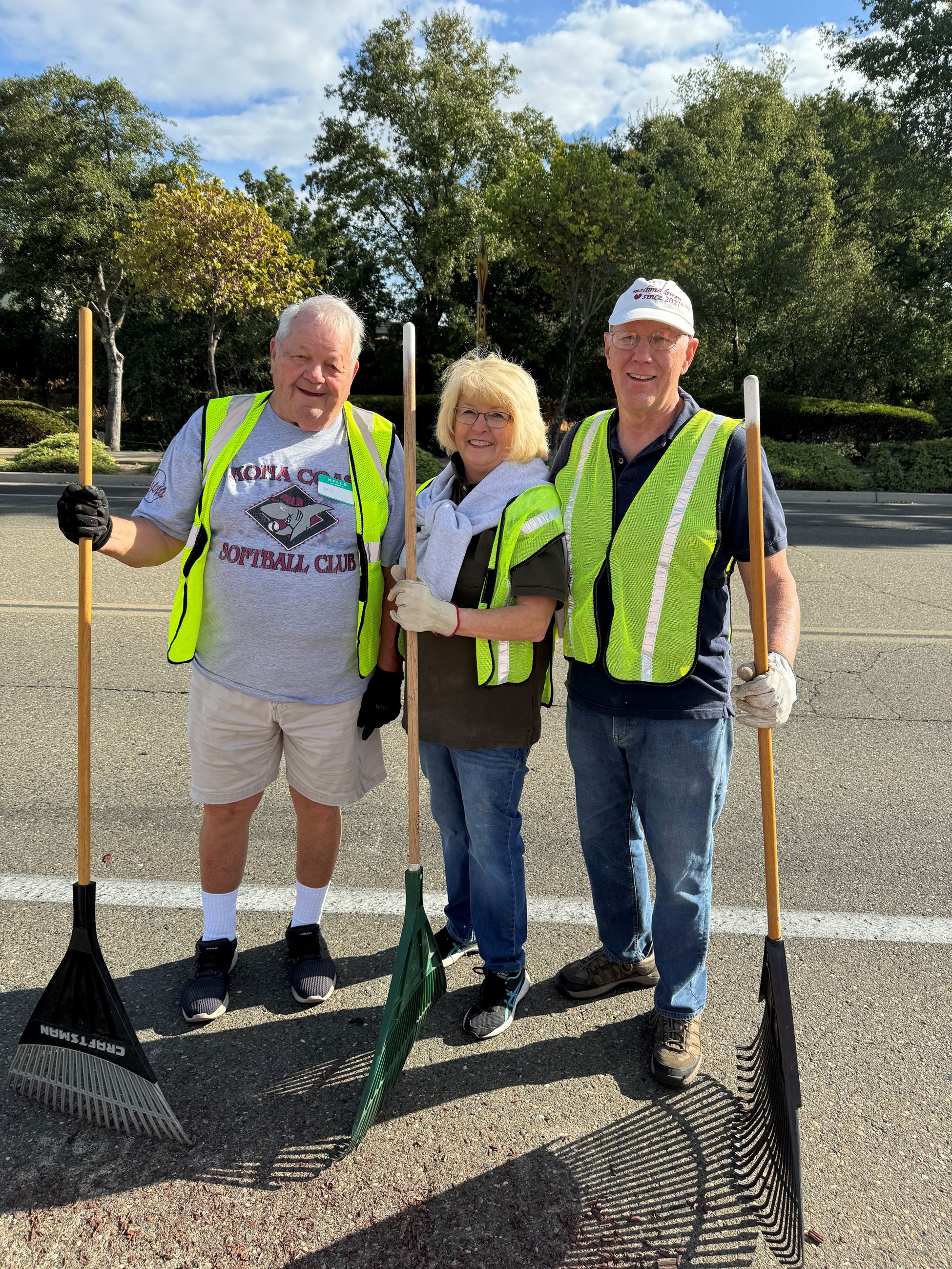 Three people pose with rakes in hand.